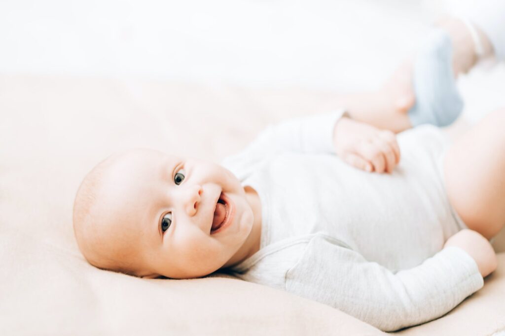 newborn laughing baby lying on the bed caring for newborn children e1634098456771.jpg
